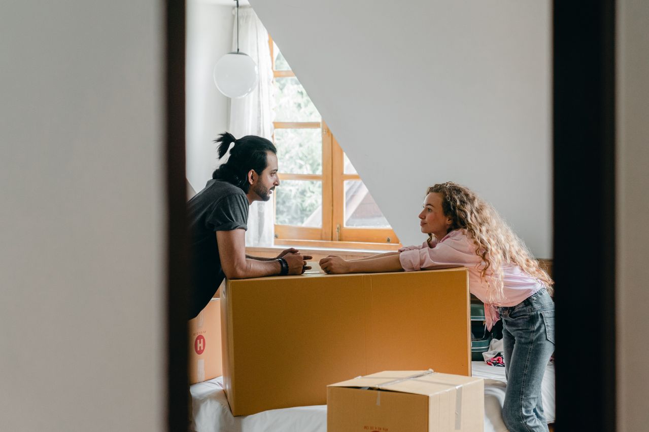 Couple talking over cardboard moving boxes in attic. 