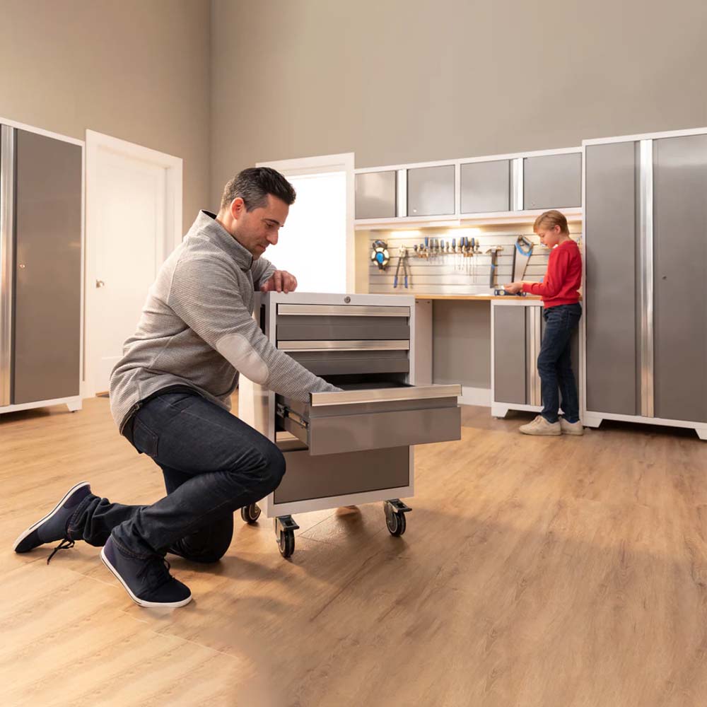 A Man Adjusting The NewAge Bold Series 6 Piece Cabinet Set With Tool And 30 In Locker While A Young Child Explores A Workbench