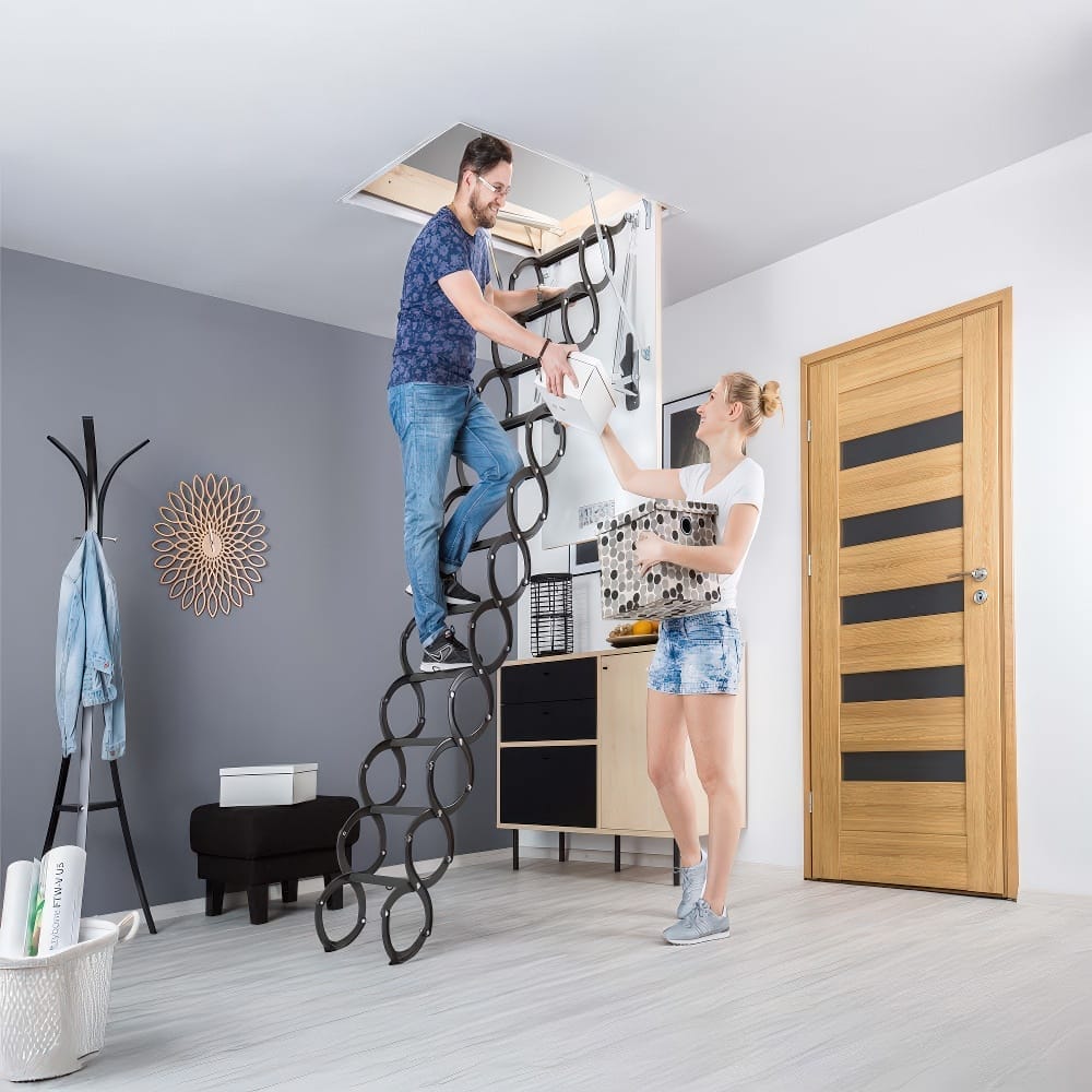 A Man And Woman Are Working Together To Pass Storage Items Up A Retractable Scissor Attic Ladder
