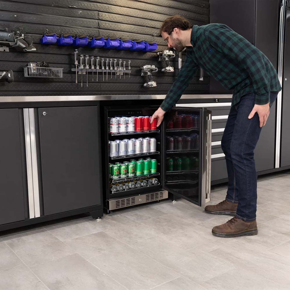 A Man Reaches Into A Glass-Door Beverage Cooler Built Into A Sleek Garage Workstation Surrounded By Organized Tools Bins And Power Equipment