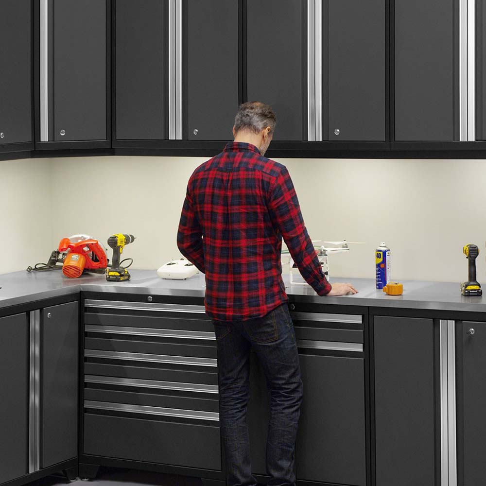A Man Stands At NewAge 16 Piece Garage Cabinet Corner Set Pro 3.0 Series Surrounded By Black Cabinets And Various Tools