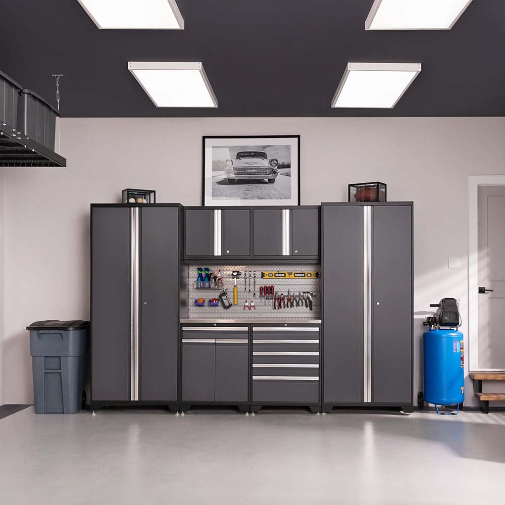 A Modern Garage Workspace With Tall Grey Storage Cabinets A Central Tool Wall Over A Workbench And Overhead Ceiling Lights