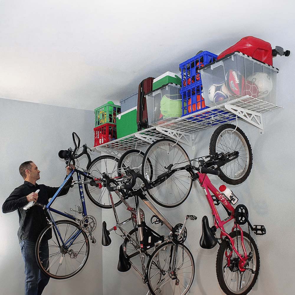 A Person Is Organizing Bicycles On A SafeRacks Wall Shelves With Hooks Beneath A Ceiling Shelf Filled With Various Storage Bins And Crates