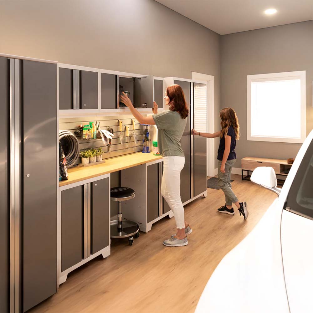 A Woman And A Child Organizing A Well-Lit Garage Workspace With Wall-Mounted And Base Cabinets A Wooden Workbench And Various Tools And Supplies Neatly Arranged On A Slatwall System