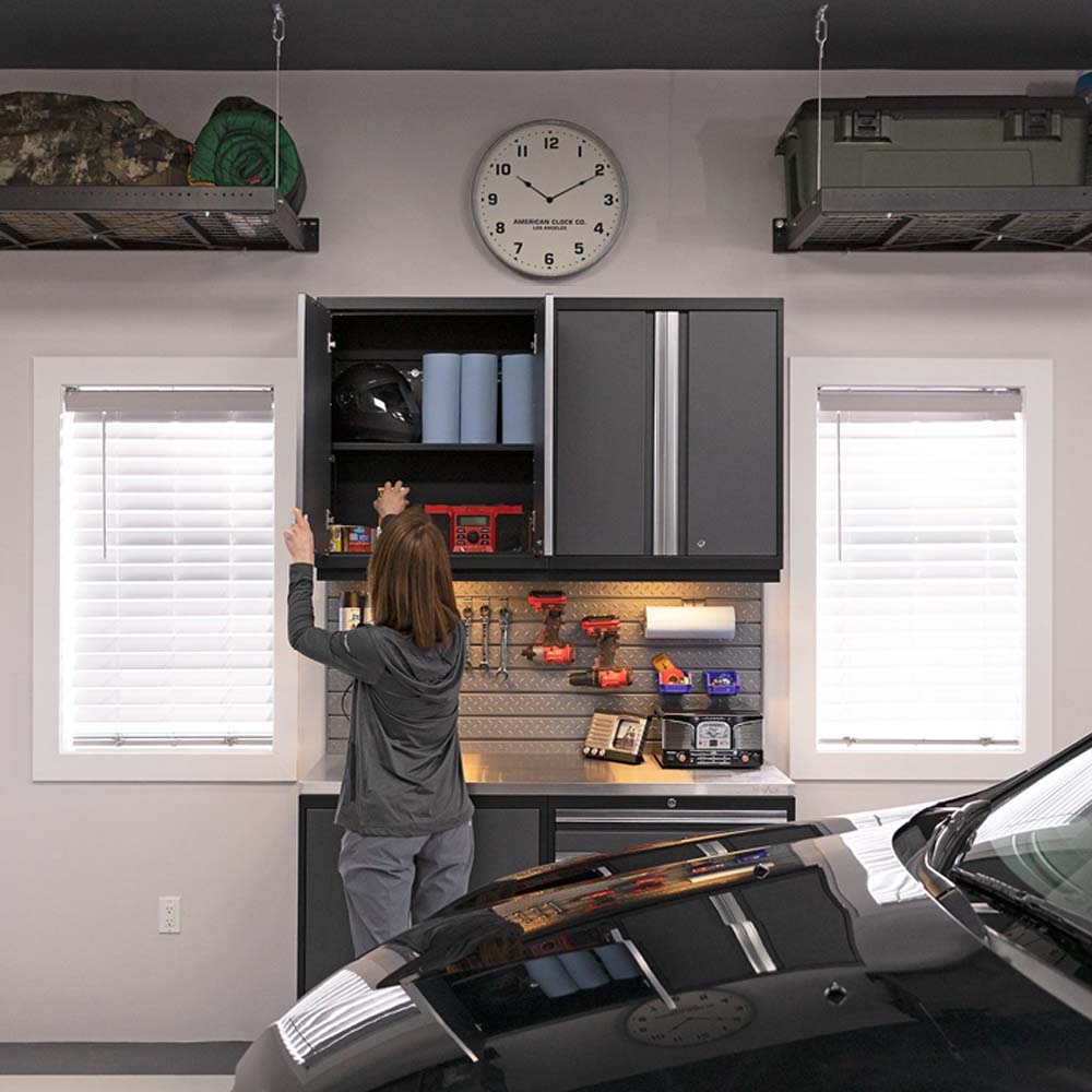A Woman Reaches Into Extra Wide 42 Inch Wall Cabinets Pro 3.0 Above A Workbench Filled With Various Tools And Equipment
