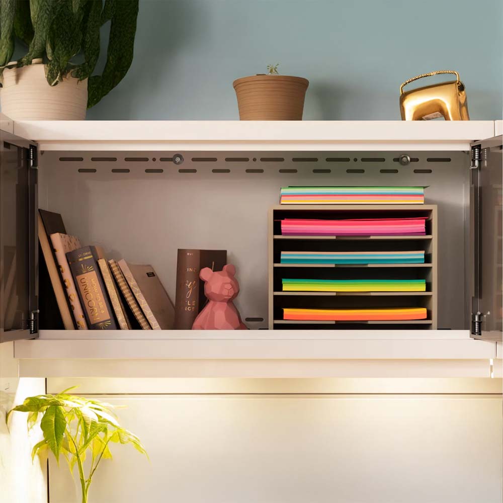 An Open Cabinet Shelf Containing Books A Pink Bear Figurine And A File Organizer Filled With Brightly Colored Paper With Potted Plants And A Gold Decor Item Placed On Top Of The Cabin