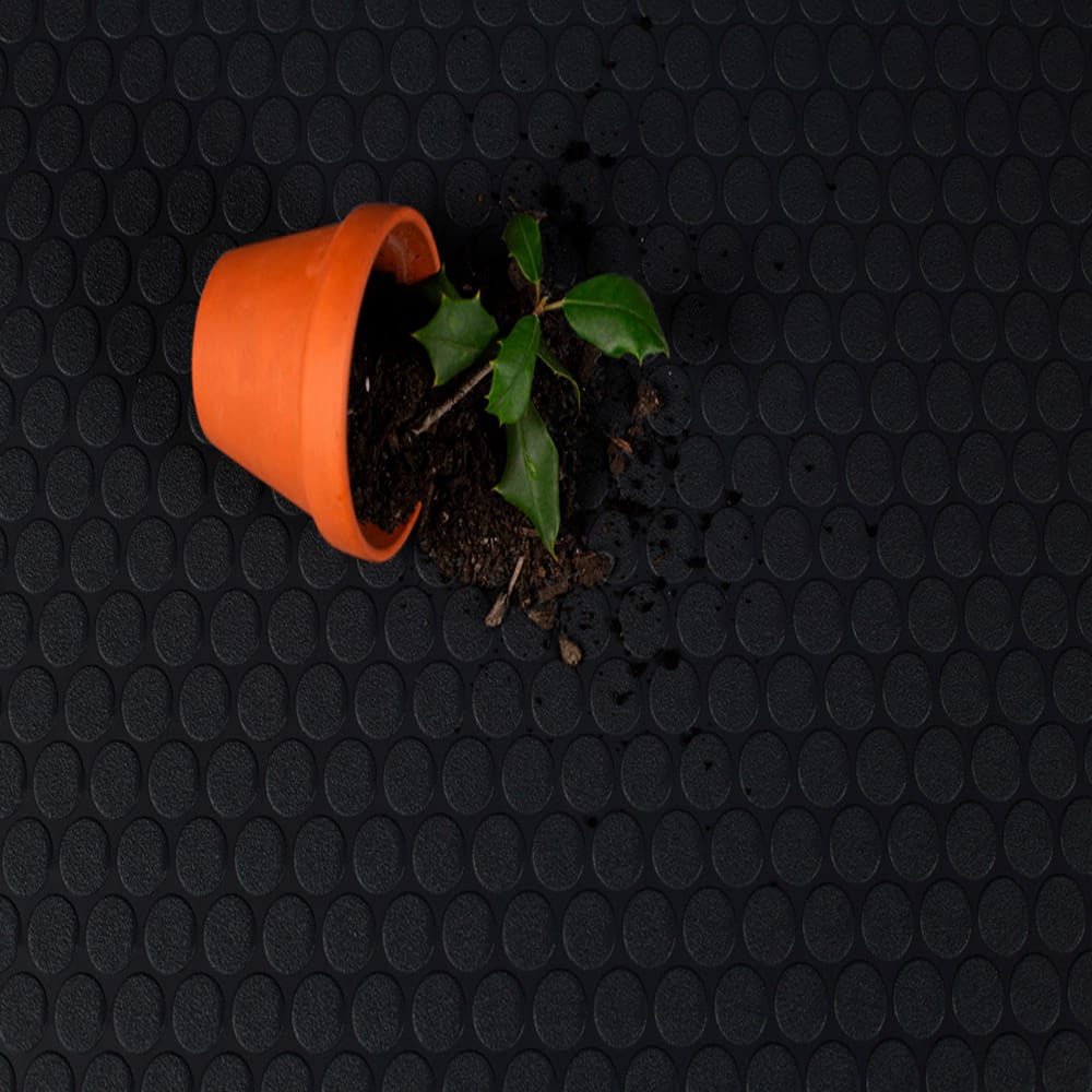 An Overturned Terracotta Pot Spills Dark Soil And A Small Green Plant Onto A Black Textured Rubber Shed Flooring