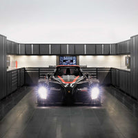 Black Race Car With Headlights On Is Parked In The Center Of A High-End Garage Outfitted With Modern Black Cabinetry