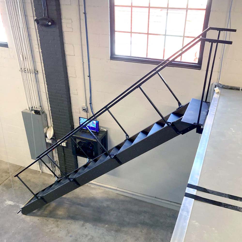 Black Steel Floating Staircase Connecting A Mezzanine Level Inside A Modern Industrial Workspace