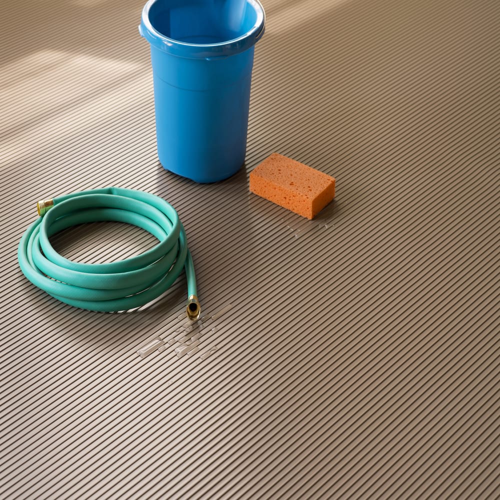 Blue Bucket A Coiled Green Hose And An Orange Sponge Placed On A Ribbed Floor With A Small Puddle Of Water