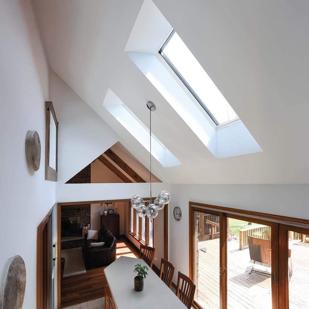 Bright Kitchen Interior With Slanted Ceiling Two Skylights A Glass Ball Chandelier And Wooden Sliding Doors Leading To Deck
