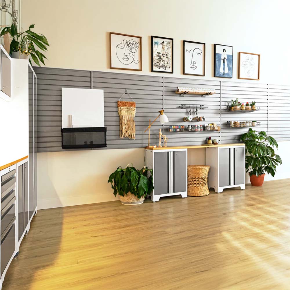 Bright Organized Craft Room With Gray Slatwall Panels Framed Art Above Potted Plants On The Floor Storage Cabinets Below A Wooden Worktop And Shelves