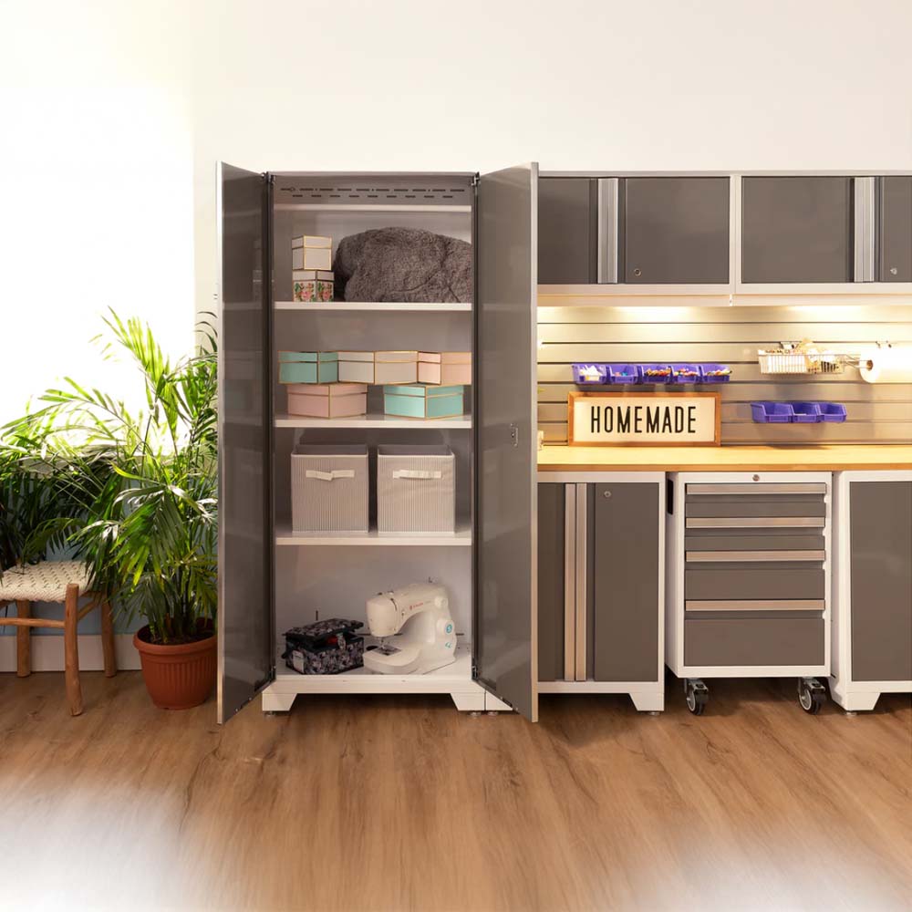 Brightly Lit Crafting Area With An Open Tall Cabinet Containing Storage Boxes Fabric And A Sewing Machine Next To A Workbench