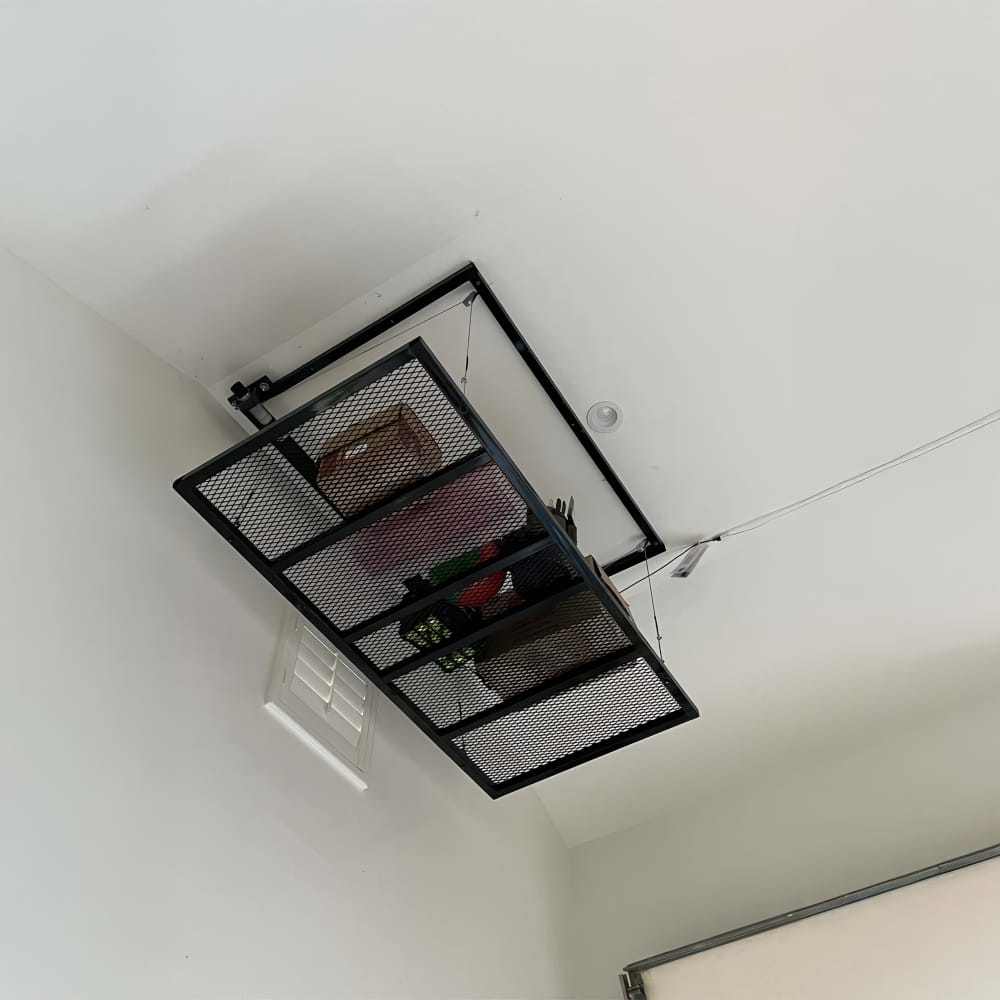 Ceiling Mounted Metal Overhead Storage Rack With Mesh Shelf Holding Boxes And Gear In A Garage