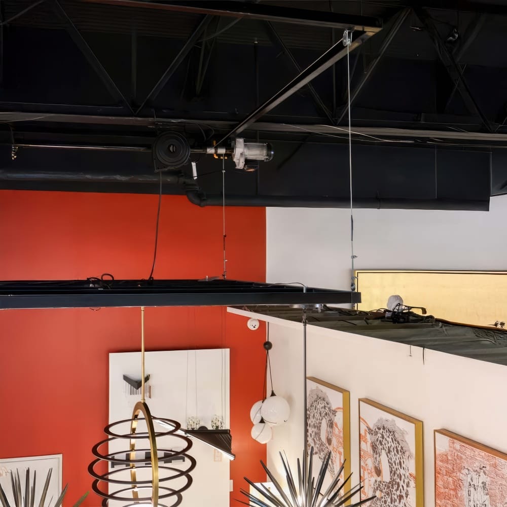 Ceiling Mounted Motorized Hoist System With Cables Suspends Lighting Fixtures Above A Modern Showroom With Red Accent Wall