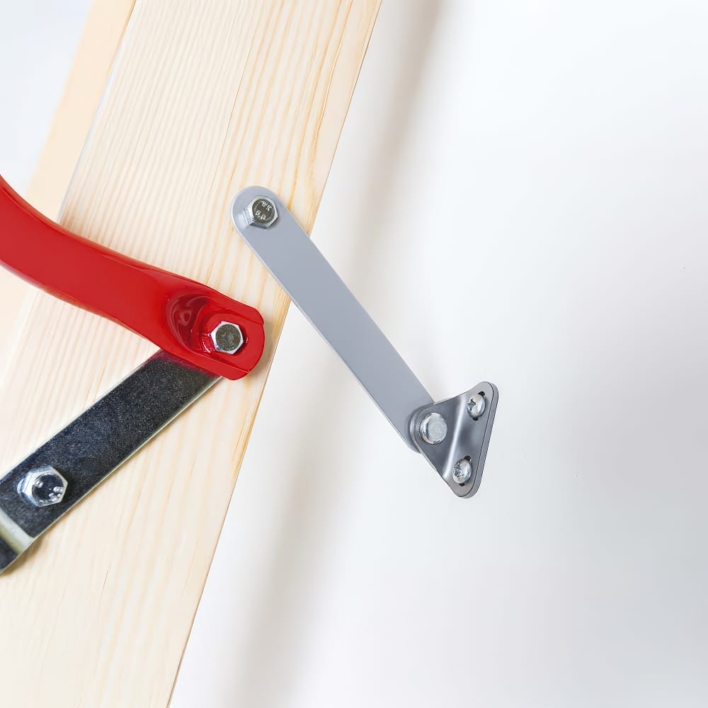 Close-Up Of A Metal Hinge And Support Arm Assembly Secured With Bolts To A Wooden Attic Ladder And Its White Access Panel