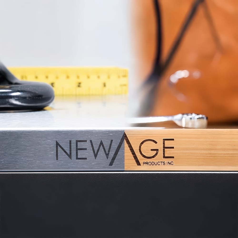 Close-Up Of A NewAge Products Inc. Logo Engraved On A Wood-And-Metal Workbench Surface With Tools And A Yellow Measuring Tape