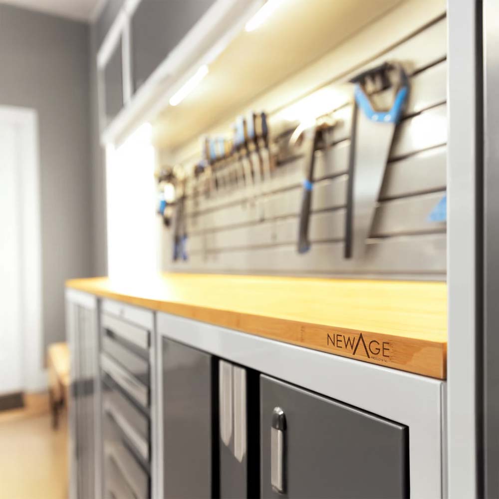Close-Up Of A Well-Organized Garage Workspace Featuring A Bamboo Worktop Branded With The NewAge Logo Metal Cabinets Below And A Slatwall With Hanging Tools