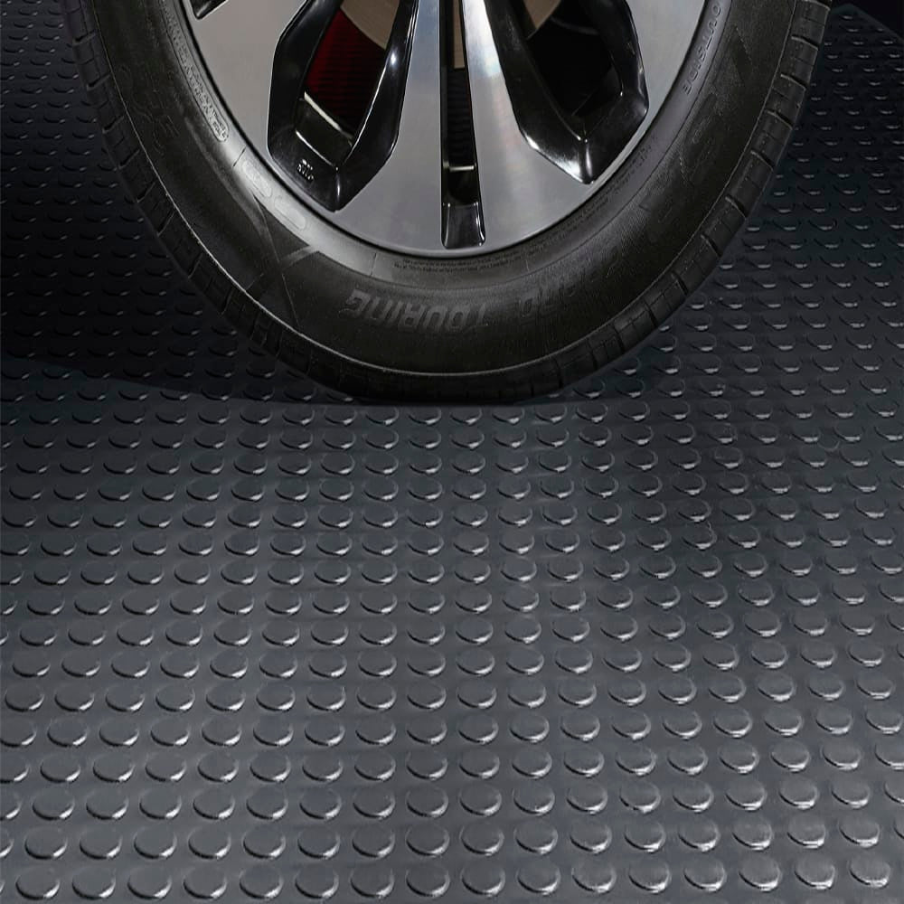 Close Up View Of A Black Tire With A Shiny Alloy Wheel Resting On A Textured Rubber Large Coin Flooring With A Circular Pattern