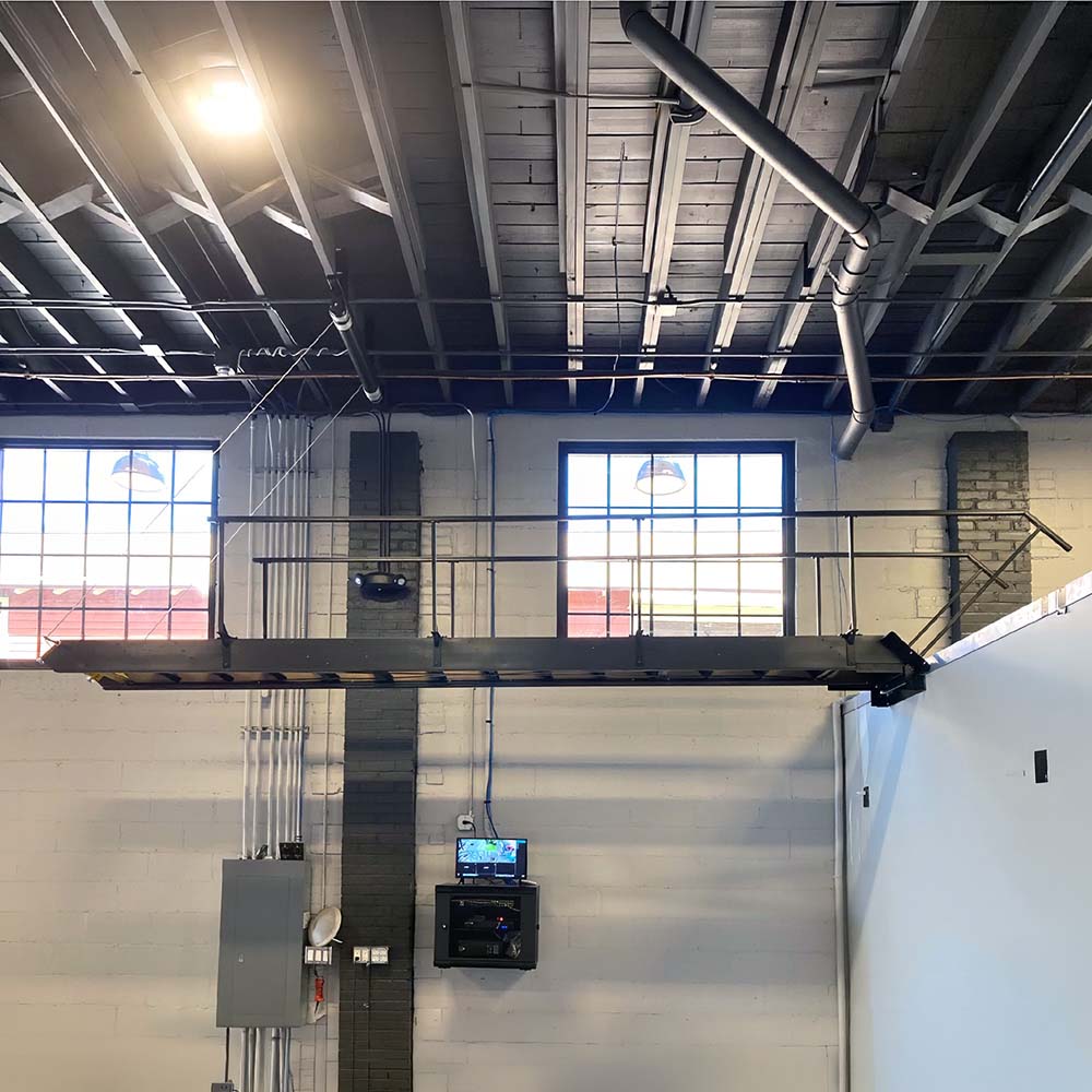 Elevated Steel Walkway Suspended Between Industrial Walls Beneath An Exposed Warehouse Ceiling