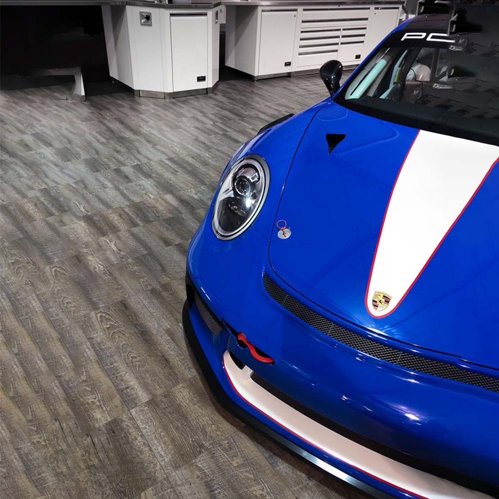 Front Portion Of A Vibrant Blue Sports Car With A White Racing Stripe Parked In A Garage And A Race Deck Smoked Oak Flooring