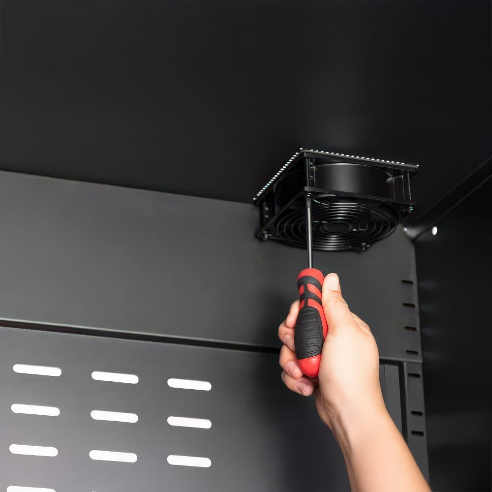 Hand Using A Screwdriver To Install A Cooling Fan Inside A Black Metal Cabinet