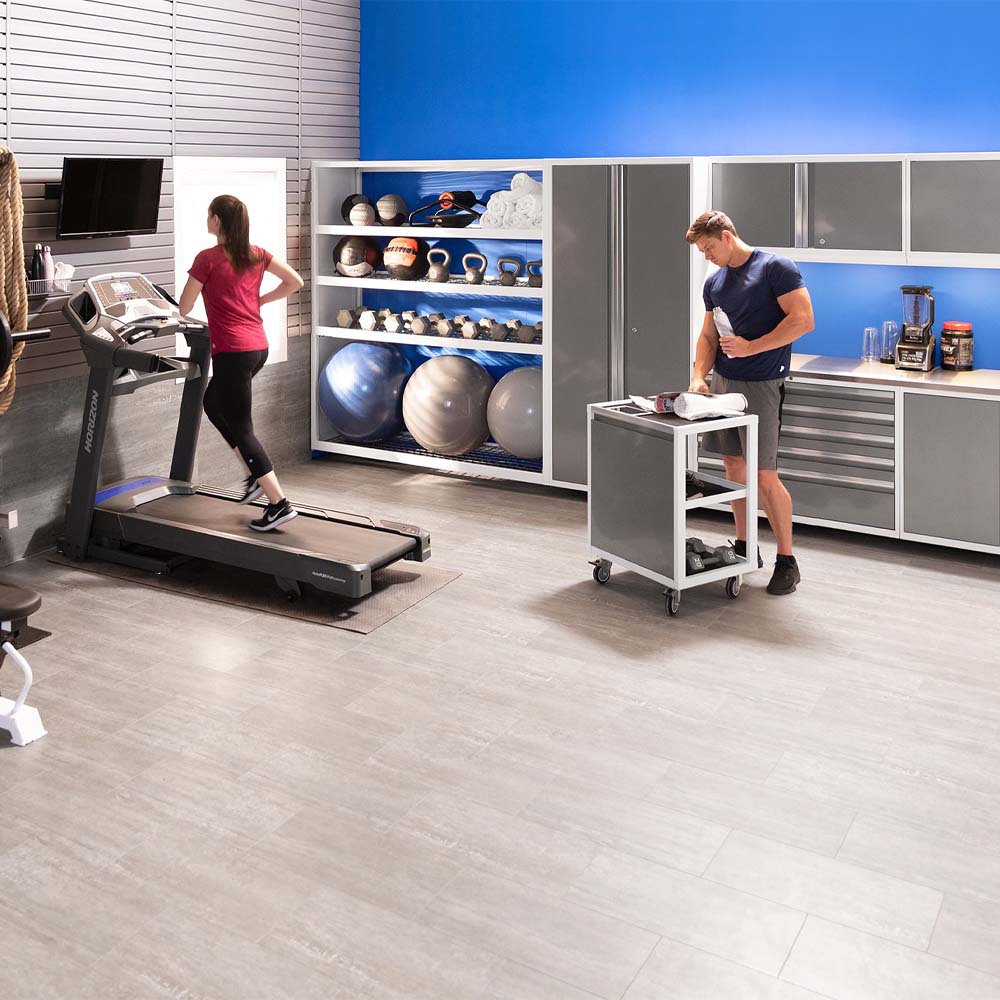 Home Gym With Woman Running On Treadmill And Man Preparing Equipment Beside Shelving And Cabinet Storage