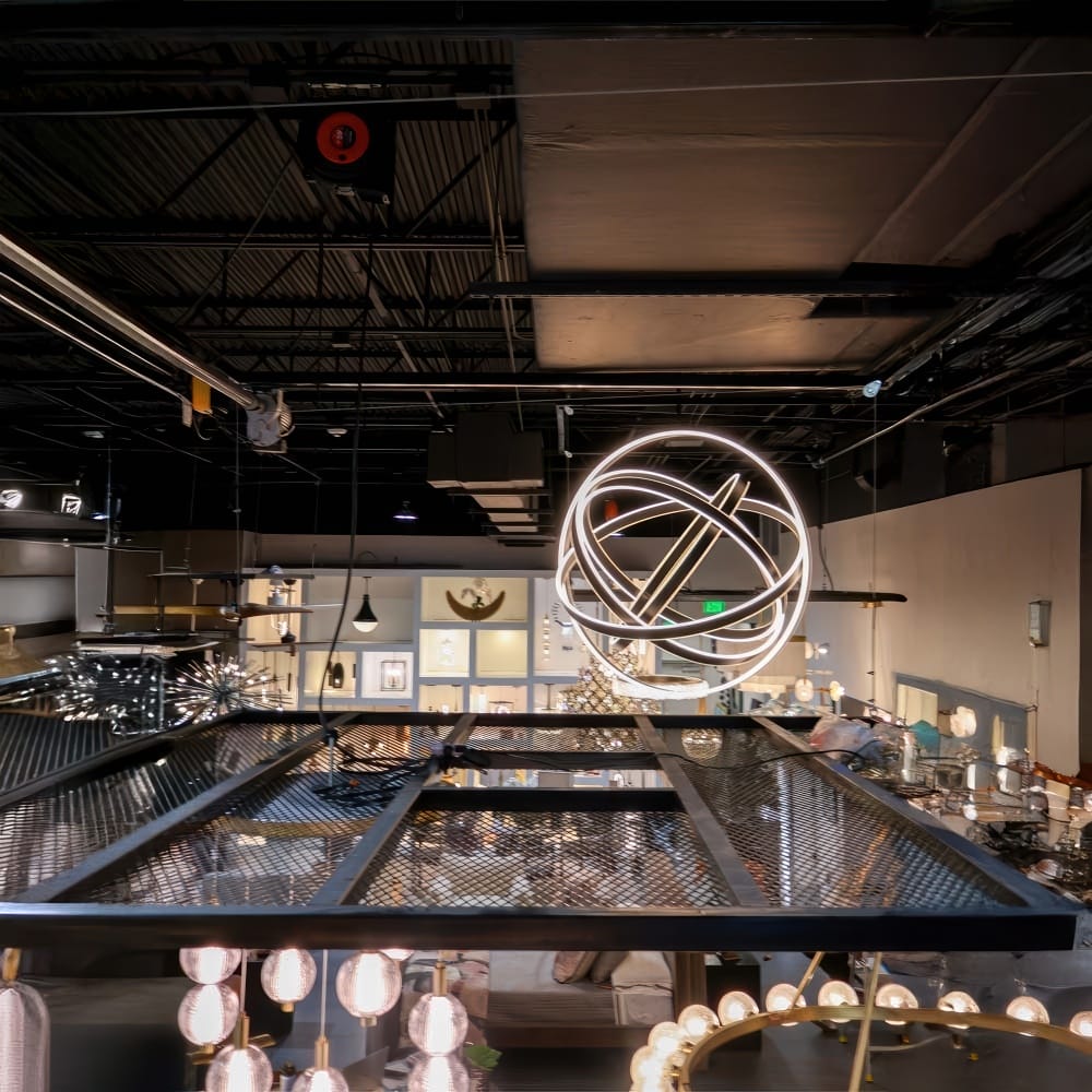 Illuminated Spherical LED Chandelier Hangs Over A Mesh Ceiling Platform In A Modern Lighting Showroom