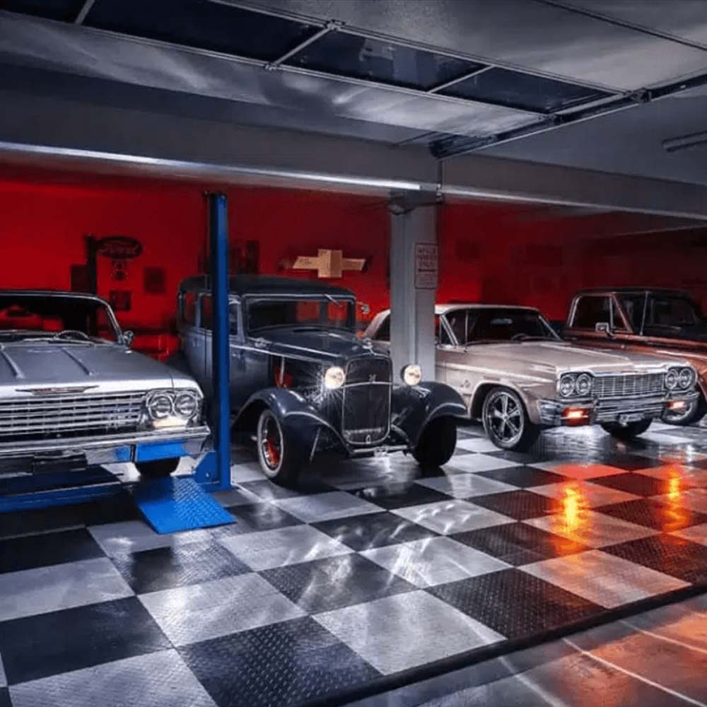 Lit Garage Filled With Classic Cars All Set Against A Backdrop Of Red Walls, A Checkered Race Deck Tuffshield Garage Flooring, And Exposed Metal Beams Overhead