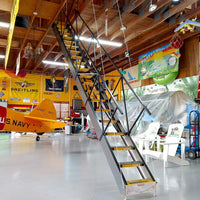 Majic Sliding Attic Stairs With Yellow Steps Is Set In An Airplane Hangar