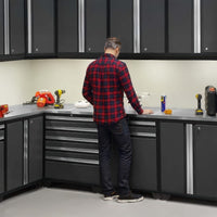 Man Standing At L Shaped Workbench Surrounded By Tall Cabinets And Drawers In A Modern Garage