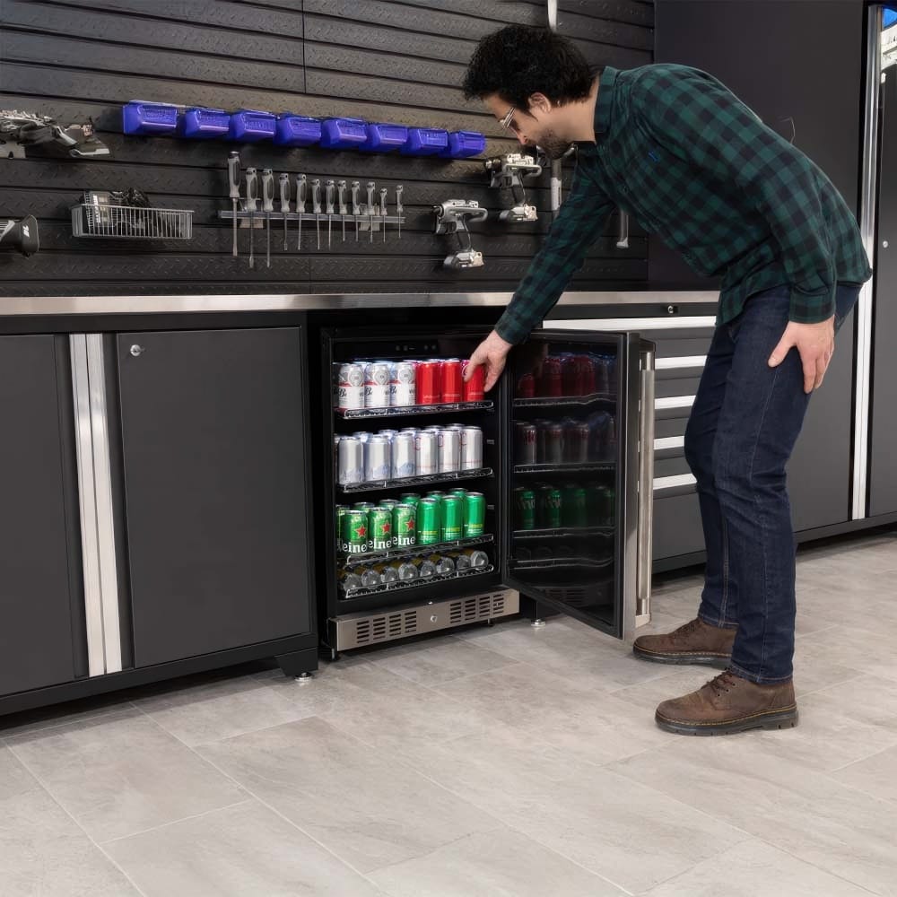 Man Stocks A Beverage Mini Fridge Built Into A Garage Workbench With Tools Displayed On A Slatwall Backdrop