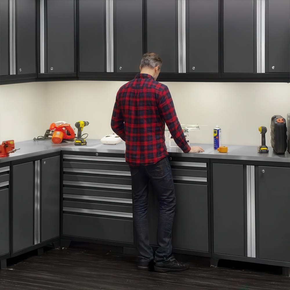 Man Working At Corner Garage Workbench With Grey Cabinets And Power Tools On The Countertop