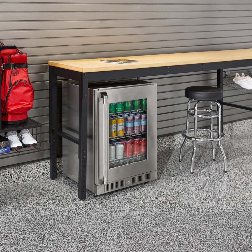 Modern Garage Setup With A Long Wooden Workbench A Stainless Steel Glass-Door Beverage Fridge Stocked With Cans A Chrome Bar Stool And Organized Gear 