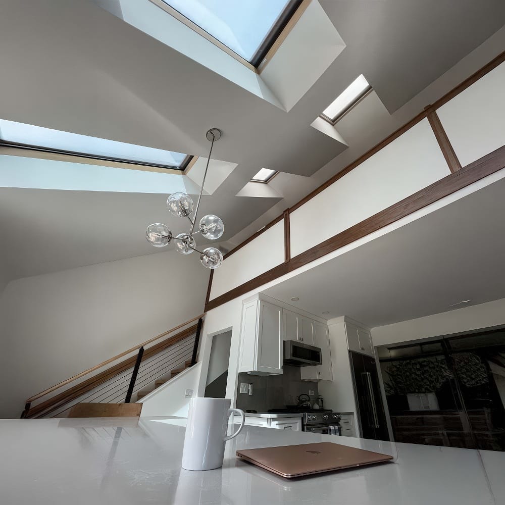 Modern Kitchen With Skylights A White Countertop A Coffee Mug A Laptop And A View Of Stairs And Wooden Railing