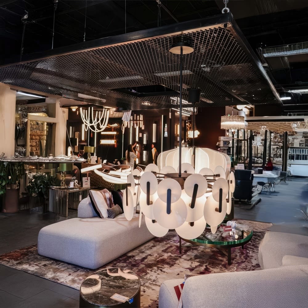 Modern Lighting Showroom Featuring Sculptural Chandeliers Plush Sectionals And Contemporary Decor Under An Industrial Mesh Ceiling