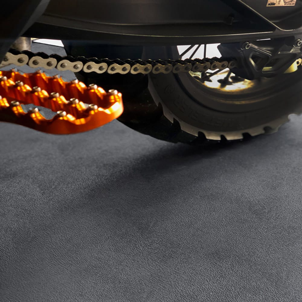 Motorcycles Rear Section Featuring The Chain Sprocket And A Bright Orange Footpeg Against A Black G-Floor Garage Flooring
