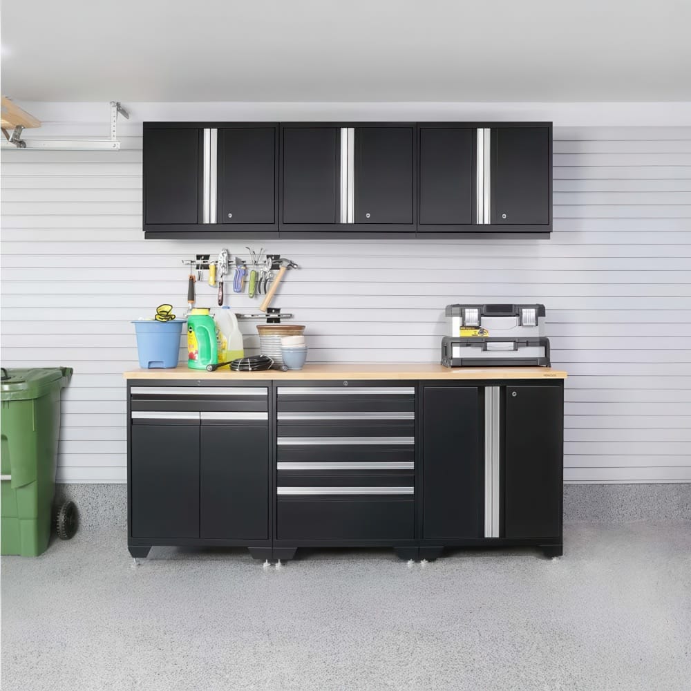 Organized Garage Workstation With Black Wall Cabinets Slatwall Tool Hooks And A Black Base Cabinet With Wooden Worktop Next To A Green Trash Bin