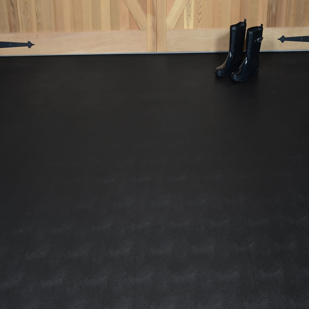 Pair Of Black Rain Boots Placed On A Smooth Dark G-Floor Levant Mat In Front Of A Wooden Wall With A Barn Style Door