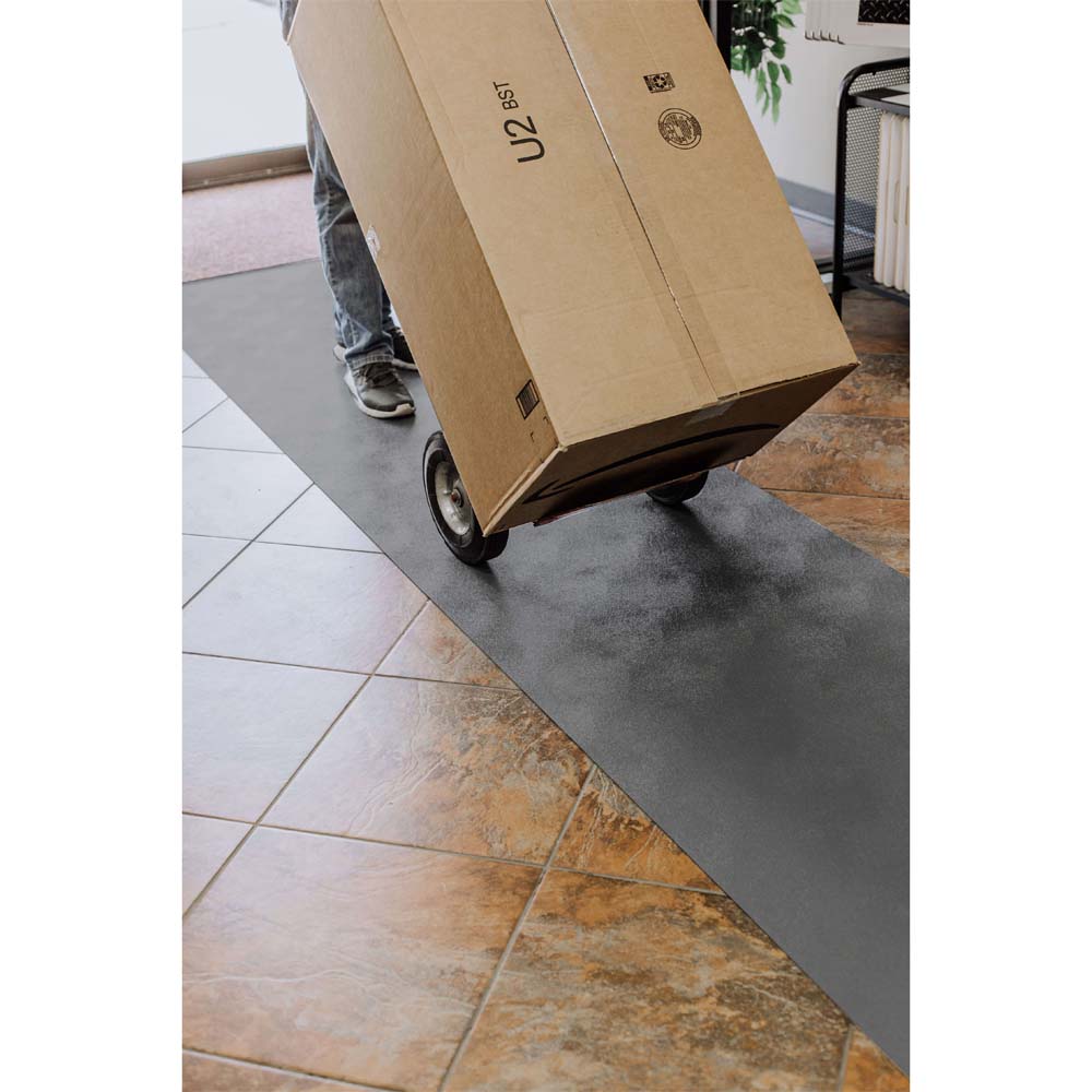Person Using Wheeled Dolly To Transport A Large Cardboard Box Across A Runner Floor Mats G-Floor
