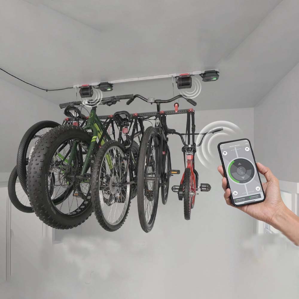 Person&#39;s Hand Holds A Smartphone With A Control App In Front Of Bicycles Hung From A Ceiling Rack By SmarterHome Garage Lifter
