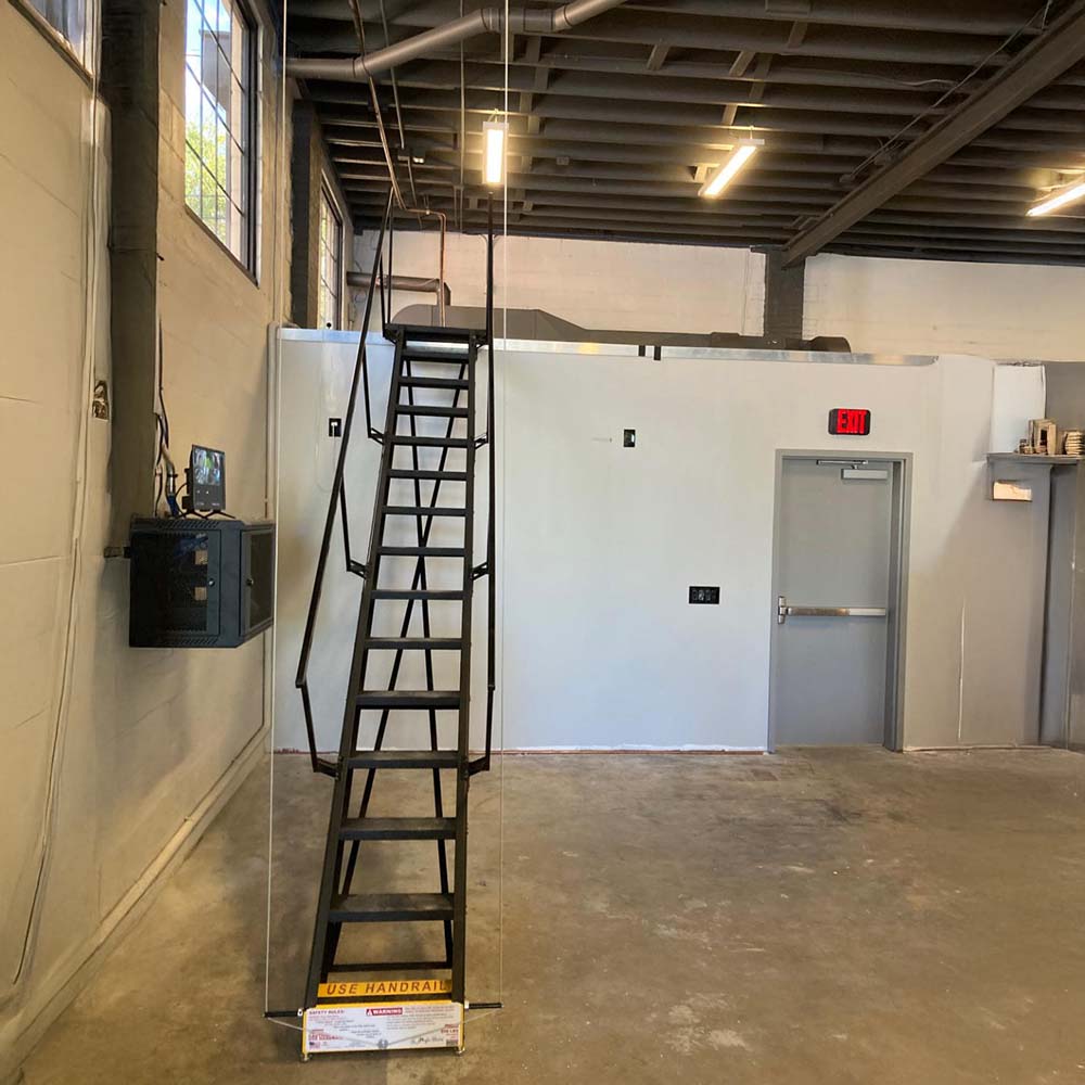 Retractable Black Steel Stairway Extending To An Elevated Mezzanine Inside An Industrial Building