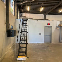 Retractable Black Steel Stairway Extending To An Elevated Mezzanine Inside An Industrial Building