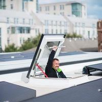 Smiling Man Climbing Through Rooftop Skylight With Solar Panels Around