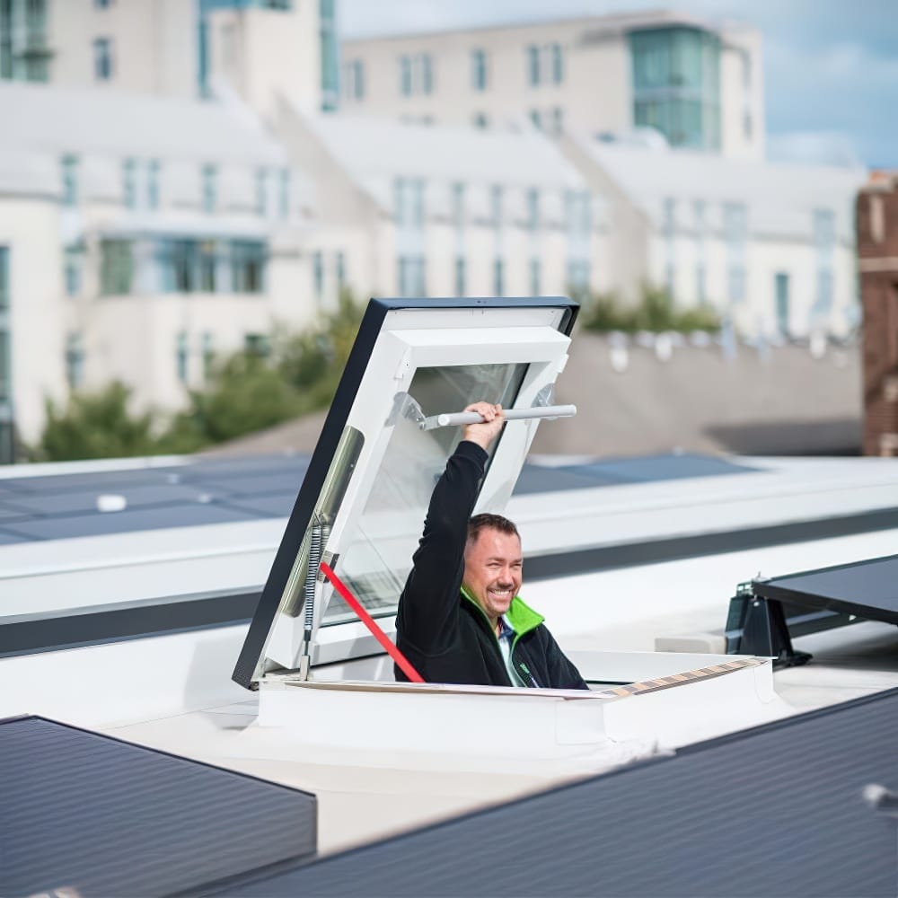 Smiling Man Climbing Through Rooftop Skylight With Solar Panels Around