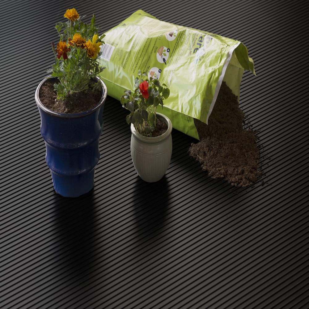 Two Potted Plants One In A Blue Pot With Yellow And Orange Flowers And The Other In A White Pot With A Red Flower Placed On G-Floor Ribbed Garage Flooring
