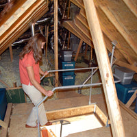 Woman In An Attic Interacting With A Lifting System Amidst Insulation And Storage Containers Under A Wooden Beam Structure