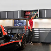 Woman In Red Shirt Reaches Into Overhead Garage Cabinet Beside A Race Car In A Sleek Workshop