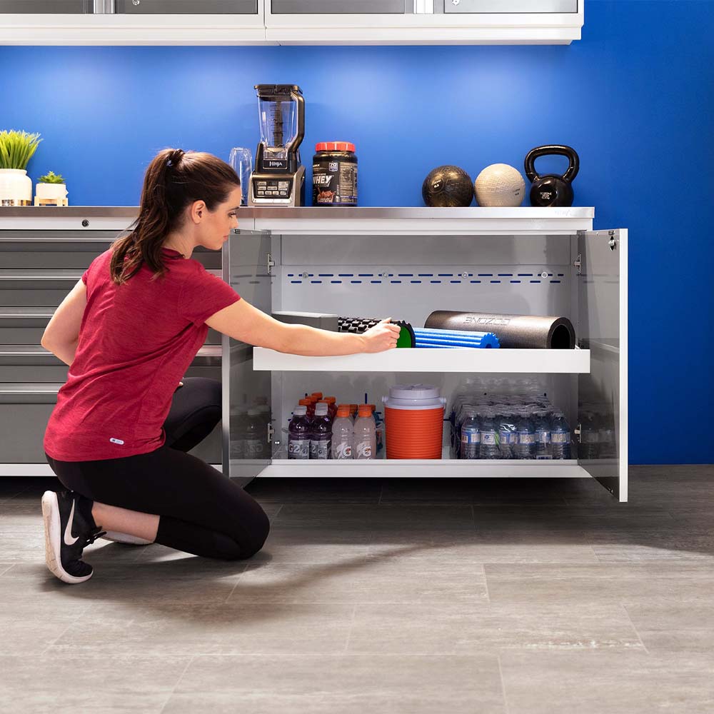Woman Organizing Fitness Gear And Sports Drinks In A White Gym Cabinet Below A Blue Wall