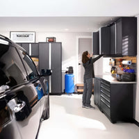 Woman Reaches Garage Wall Cabinets In Organized Workspace With Black Car Blue Air Compressor And Tool Bench